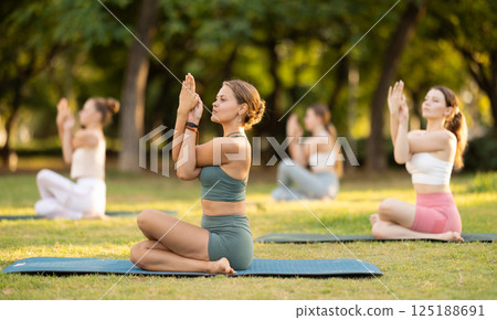 Yoga training in summer sunny park - girls in kagasana pose on mats 125188691