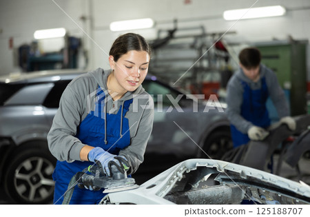 Young woman auto mechanic polishes body parts by car buffer polisher machine tool 125188707