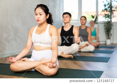 Young Asian lady performs comfortable lotus asana-Padmasana-Siddhasana pose 125188717