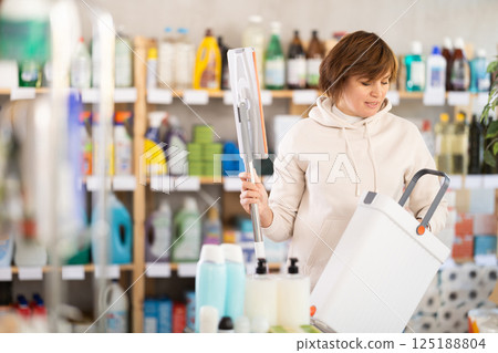 Store visitor woman purchases in household chemicals department, choose mop with plastic bucket 125188804