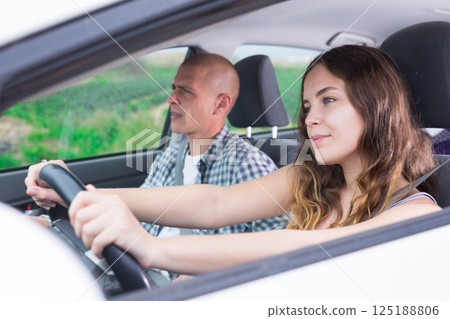 Confident young woman driving car with man in passenger seat Confident young woman driving car with man in passenger seat 125188806