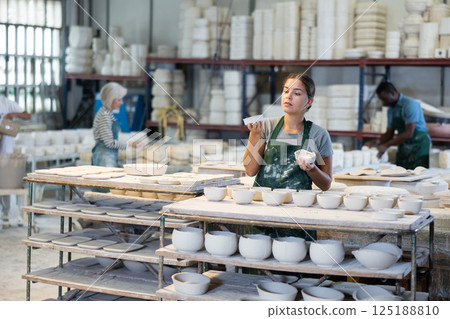 Girl ceramist arranging new bowls in workshop Girl ceramist arranging new bowls in workshop 125188810
