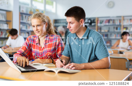 European schoolgirl with a classmate in the library is preparing for lessons 125188824