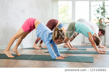 Diligent little girl practicing downward facing dog pose of yoga with her family 125188882