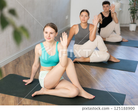 Woman and man performing Ardha Matsyendrasana position during group yoga training in fitness gym 125188900