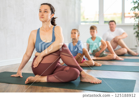Adult woman with family practicing yoga in studio 125188912