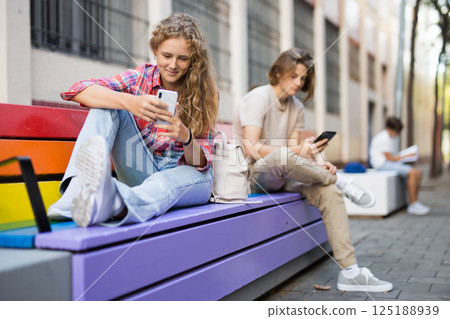Teenagers sitting on bench and using smartphones 125188939