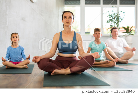 Positive pre-teen girl performing yoga exercises with brother and parents at gym 125188940