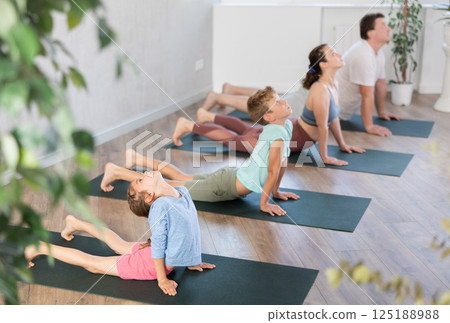 Pleasant little girl practicing cobra pose of yoga with her family Pleasant little girl practicing cobra pose of yoga with her family 125188988