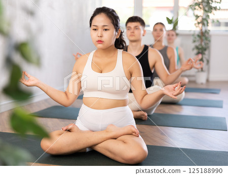 Young yogi girl and man making yoga meditation in lotus pose in fitness studio 125188990