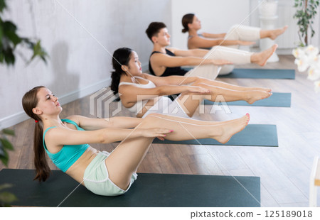Slim young girl practicing boat pose of yoga on black mat Slim young girl practicing boat pose of yoga on black mat 125189018