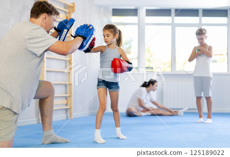Girl and dad are boxing in gym, father helps child to work out force of blow. Girl and dad are boxing in gym, father helps child to work out force of blow. 125189022