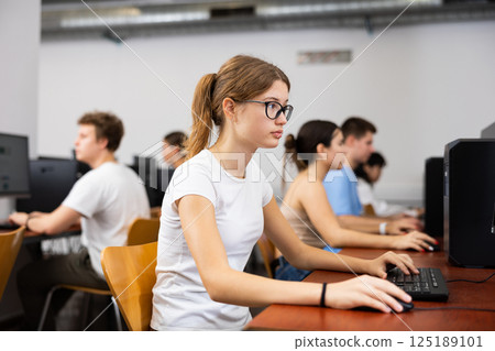 Clever female teenager wearing glasses and solving tasks of computer science in the auditory 125189101