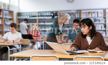 Schoolgirl studies on a laptop and writes notes in a copybook 125189224