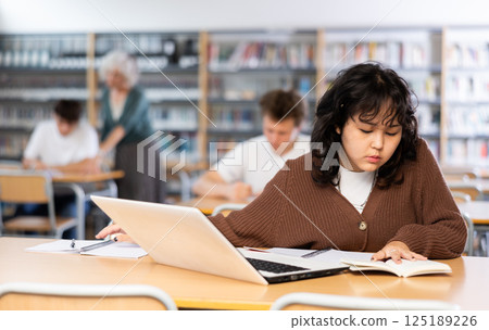 Asian teenager girl with a laptop studying in school library Asian teenager girl with a laptop studying in school library 125189226