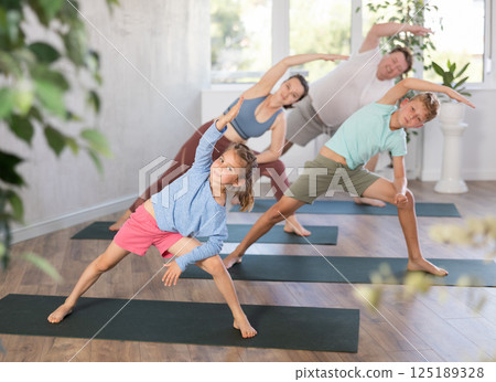 Family with children performs physical education lateral elongated angle pose, Parshvakonasana. Family with children performs physical education lateral elongated angle pose, Parshvakonasana. 125189328