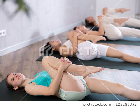 Groupd og young people doing reclining twist yoga pose in studio. 125189352