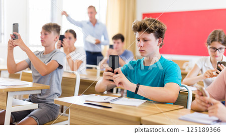Students using mobile phones and writing in notepads during lesson closeup Students using mobile phones and writing in notepads during lesson closeup 125189366