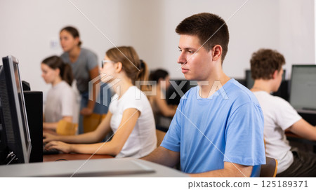 Side view on concentrated teenager male student sitting at library desk, preparing for exam in computer class 125189371