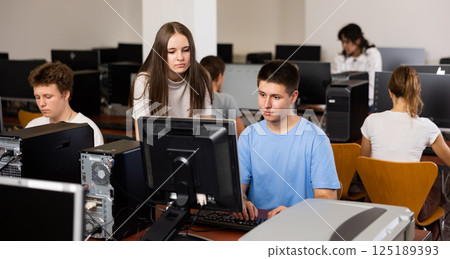 Concentrated female student explaining the topic to male friend while she is studying computer science on the pc in the classroom 125189393