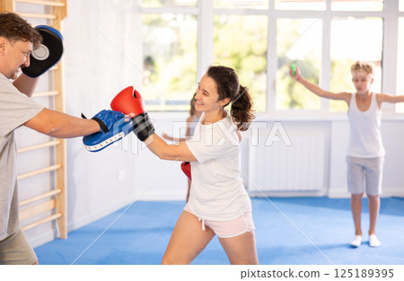 Positive woman in boxing gloves practicing punches on mitts with husband 125189395