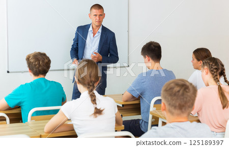 Male teacher lecturing to teenage students at auditorium Male teacher lecturing to teenage students at auditorium 125189397
