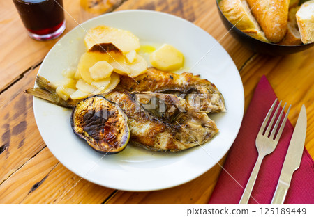 Healthy and low-calorie dish of fried dorado fish, complemented by baked potato and eggplant 125189449
