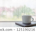 A coffee cup and a book on a rainy day window sill 125190216