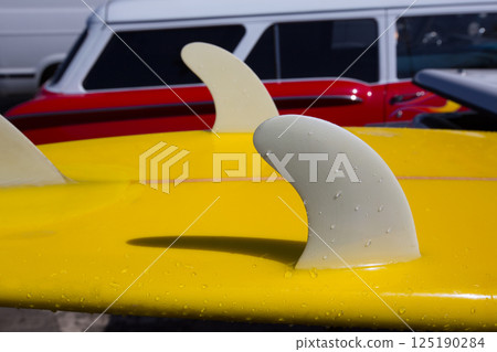 Yellow surfboard keel fins detail eith red retro car in California Yellow surfboard keel fins detail eith red retro car in California 125190284