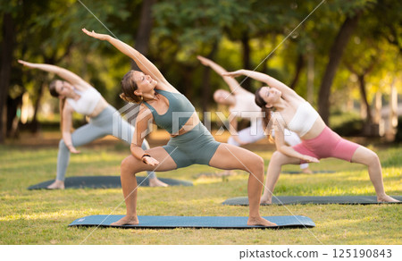 Slim women practicing yoga - virabhadrasana pose in summer park Slim women practicing yoga - virabhadrasana pose in summer park 125190843