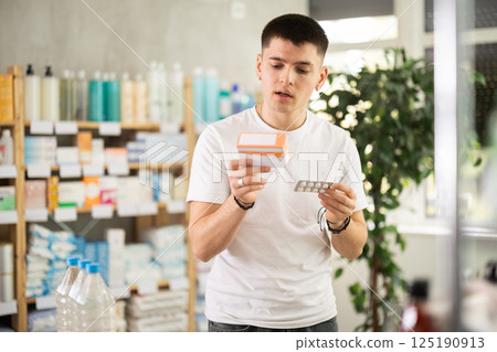 young guy chooses packages of pills in a pharmacy 125190913