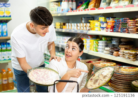 Young man and woman buying frozen pizza together in supermarket Young man and woman buying frozen pizza together in supermarket 125191136