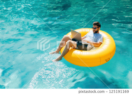 Man with laptop on inflatable ring in the water 125191169