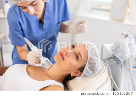 Female patient experiencing cryotherapy procedure on neck using ice hammer 125191207