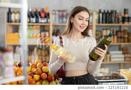 Girl buyer looks thoughtfully and indecisively at bottles of vegetable oil 125191228