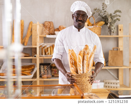 African male baker worker sells baguette, shows many products 125191238