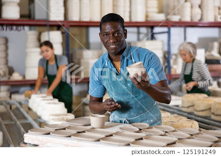 Positive man potter with new crafted crockry in workshop 125191249