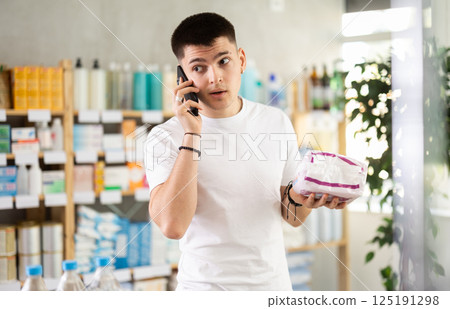 guy is holding a package of pads in his hands and making a phone call 125191298