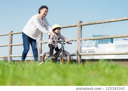 A 5-year-old boy learning to ride a bike with his father supporting him 125191341