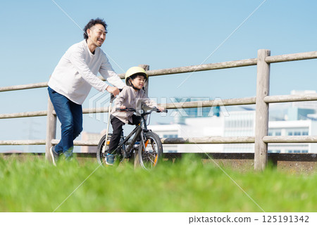 A 5-year-old boy learning to ride a bike with his father supporting him A 5-year-old boy learning to ride a bike with his father supporting him 125191342