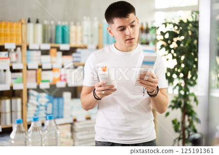 Young man choosing skin care lotion, sun protection gel or medical ointment in drugstore 125191361