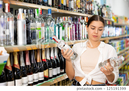 in hard liquor department, young woman carefully chooses vodka 125191399