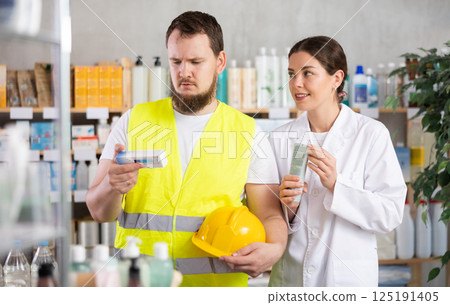 Laboring man builder buys gel for burns at pharmacy, consulting with girl pharmacist 125191405