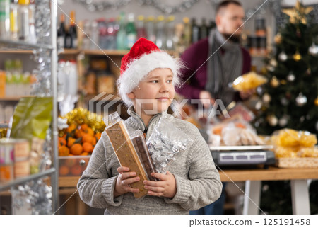 Little boy holding turrons and other sweets in market with Xmas decoration Little boy holding turrons and other sweets in market with Xmas decoration 125191458