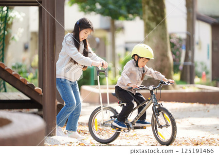 A 10-year-old sister helps her 5-year-old brother learn to ride a bike A 10-year-old sister helps her 5-year-old brother learn to ride a bike 125191466