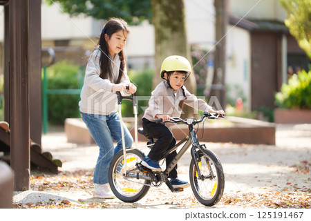 A 10-year-old sister helps her 5-year-old brother learn to ride a bike A 10-year-old sister helps her 5-year-old brother learn to ride a bike 125191467