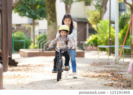 A 10-year-old sister helps her 5-year-old brother learn to ride a bike 125191469