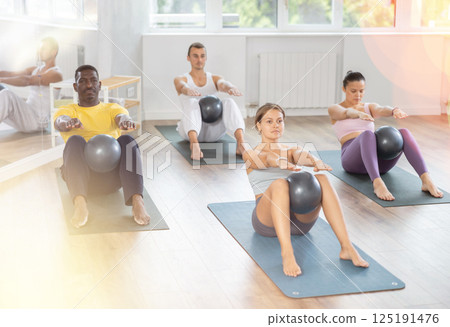Multiethnic group of people doing exercises for press with pilates ball during group class in fitness gym Multiethnic group of people doing exercises for press with pilates ball during group class in fitness gym 125191476
