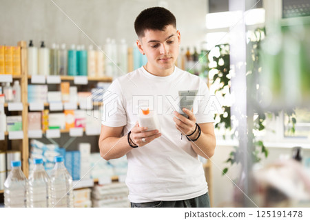 Young man choosing skin care lotion, sun protection gel or medical ointment in drugstore Young man choosing skin care lotion, sun protection gel or medical ointment in drugstore 125191478