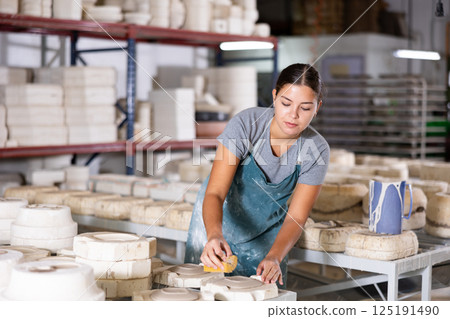Female ceramist wiping clay bowl with sponge in ceramic factory Female ceramist wiping clay bowl with sponge in ceramic factory 125191490